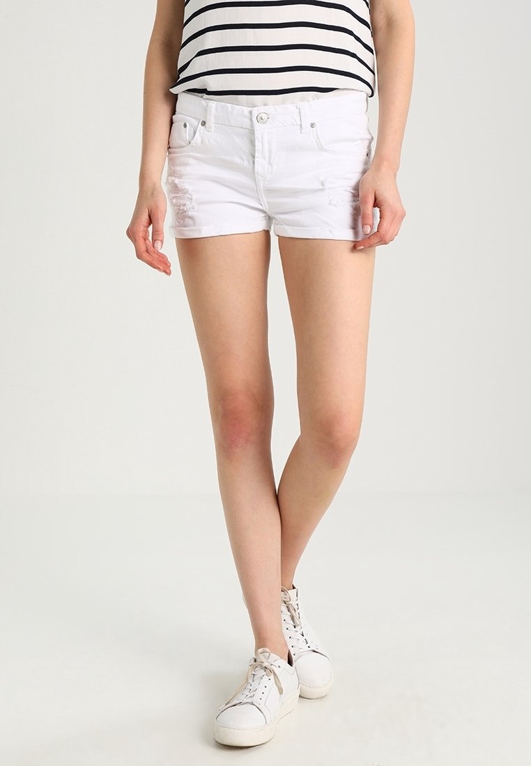 Shorts de mezclilla blanca con detalles desgastados, diseño ajustado y estilo de cinco bolsillos. Combinados con una camiseta de rayas en blanco y negro y zapatillas blancas.