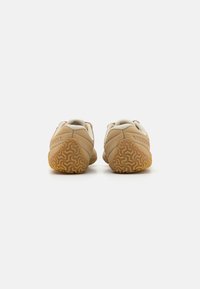 Par de zapatos Merrell marrones con suelas de goma texturizadas, cuellos acolchados y un diseño elegante y minimalista. La vista trasera muestra el detalle del logo.