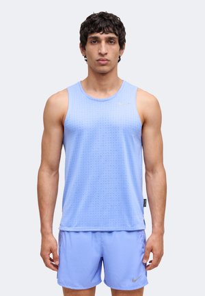Homme portant un maillot de sport sans manches bleu clair et un short assorti, debout face à un fond uni.