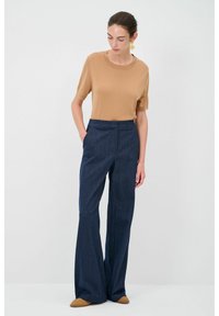Světle hnědý top s krátkými rukávy spárovaný s tmavě modrými širokými kalhotami. Tento outfit se vyznačuje hladkou texturou a upraveným střihem.