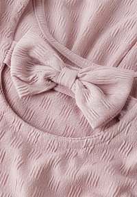 Helles rosa Gewebe mit strukturiertem, geripptem Design und einer Schleifendetail am Halsauschnitt. Weiche, glatte Textur mit gerafften Kanten.