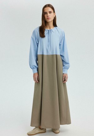 O rochie lungă, bicoloră, cu un top albastru deschis și o fustă khaki, având un guler rotund și mâneci elastice. Purtați cu teniși bej.