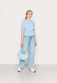 Top azul com estampado floral e mangas bufantes, jeans de perna larga em lavagem clara, bolsa em azul pastel e ténis multicoloridos com um design texturizado.
