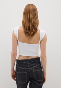 Top bianco corto con spalline larghe e schiena scoperta, abbinato a jeans in denim scuro con cuciture chiare e due tasche posteriori.