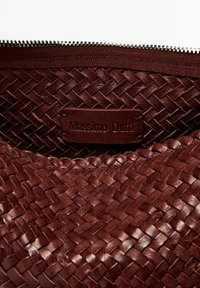 Interieur van een bruin geweven leren tas met een rits en een gemarkeerde leren label met de opdruk "Massimo Dutti." Gelaagd, duurzaam ontwerp.