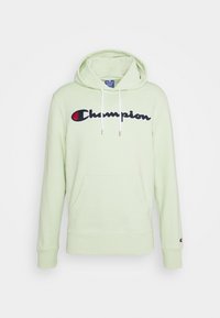 Světle zelená mikina s kapucí, klokaní kapsou, bílými šňůrkami a černě vyšitým logem "Champion" na hrudi. Měkká struktura látky.