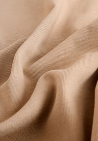 Beiger Strickstoff mit sichtbarer feiner gerippter Textur und weichen Falten, die sanfte Wellen über die Oberfläche bilden.