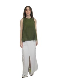 Top verde senza maniche con una vestibilità rilassata, abbinato a una gonna maxi bianca con spacco, complete di tasche laterali e dettagli con cerniera. Sneakers casual.