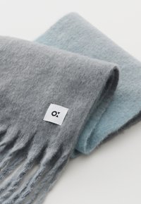 Sciarpa di lana in grigio e blu chiaro, con bordi frangiati e un'etichetta quadrata con un logo. Texture morbida e design stratificato.