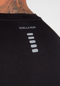 Zwarte sportshirt met "GORILLA WEAR" logo in grijs, voorzien van een gestructureerde stof en vijf horizontale grijze lijnen als designelementen.