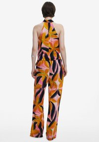Set composto da top halter multicolore e pantaloni a gamba larga. Presenta un motivo floreale nei colori rosa, arancione, verde e nero. Tessuto morbido, vestibilità comoda.