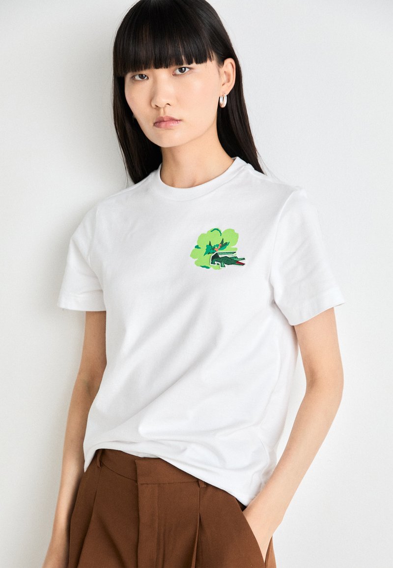 T-shirt bianca in cotone con un design grafico verde e nero, dal taglio morbido e maniche corte. Texture liscia e collo a giro classico.