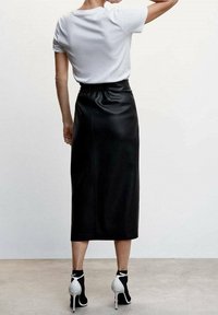 Jupe midi en cuir noir avec une taille élastique, associée à un t-shirt blanc et des chaussures à talons hautes noir et blanc en contraste.