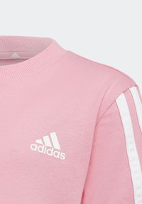 Różowy bawełniany sweatshirt z okrągłym dekoltem, strukturalnym ściągaczem i białymi trzema paskami na rękawach. Posiada białe logo Adidas.