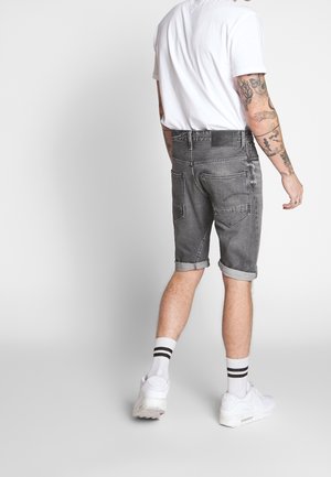 Pantalones cortos de mezclilla gris con el dobladillo enrollado, que cuentan con bolsillos traseros y una etiqueta negra en la cinturilla, combinados con zapatillas blancas y calcetines a rayas.