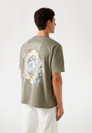 Tricou din bumbac verde măsliniu, cu imprimeu floral pe spate, cu accente albe și galbene. Mâneci scurte, croială lejeră.