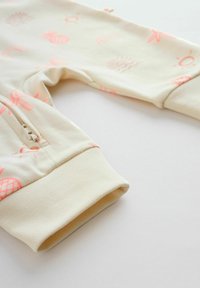Pantalon pour bébé couleur crème avec des imprimés roses sur le thème de l'été et une poche zippée latérale, montrant le bas de la jambe et les détails du poignet.