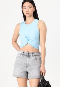 Ανοιχτό μπλε αμάνικο τοπ, με λεπτομέρεια κόμπου μπροστά, συνδυασμένο με γκρι τζιν σορτς που έχουν γυριστό τελείωμα και πλαϊνές τσέπες.