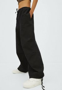 Pantalon cargo noir, ample, avec une taille élastique et un cordon de serrage, doté de poches latérales et d'une coupe droite.