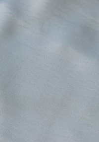 Tissu bleu clair lisse avec une texture tissée subtile et de légères ombres à la surface.