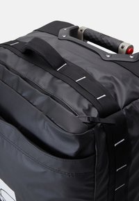 Crni ruksak s kotačima, s teksturiranim ručkom, jastučićima i kontrastnim bijelim šavovima. Ima veliki prednji džep.