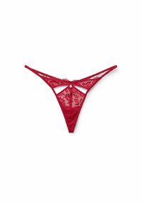 Red lace thong featuring intricate floral patterns, cut-out design at the back, and thin adjustable straps. Accented with a small silver detail.
