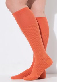 Calzini arancioni al ginocchio con una texture a coste, dotati di dettagli rinforzati nella punta e nel tallone. Tessuto liscio con una consistenza uniforme.