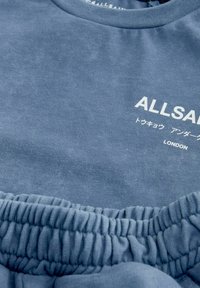 Blå bomulds sweatshirts med rund hals, elastisk talje og hvid trykt tekst, der står "ALLSAINTS LONDON." Blødt, struktureret stof.