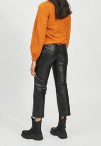 Black leather pants with a fitted design, cropped length, and subtle sheen. Paired with a textured orange sweater and black ankle boots.