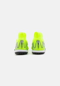 Botas de fútbol Nike Mercurial en amarillo neón vistas desde atrás, con suelas negras y patrones geométricos grises en los talones.