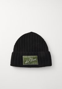 Bonnet en tricot noir à côtes avec un revers et une étiquette vert olive affichant "Les Deux" en écriture blanche. Texture lisse.