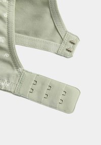 Soft green bra strap section with three-row hook-and-eye closure and floral stitching detail on light fabric background.