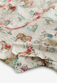 Bērnu kombinezons ar spraudņu pogām, uz kura attēlots zirgs un saimniecības motīvs maigās pasteļtoņos uz krēmkrāsas fona.