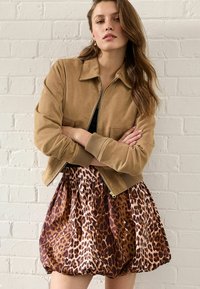 Béžová suede bomber bunda s pružnými manžetami a dolním lemem, spárovaná s volnou sukní s hnědým a oranžovým leopardím vzorem.