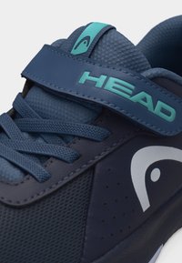Αθλητικό παπούτσι σε σκούρο μπλε χρώμα, με ύφασμα από δίχτυ, κορδόνια, τιρκουάζ λουράκι Velcro με το λογότυπο "HEAD" και λευκό στυλιζαρισμένο λογότυπο στο πλάι.