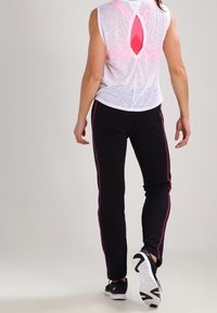 White sleeveless top with a pink cutout detail at the back, paired with black pants featuring pink side stripes and black athletic shoes.