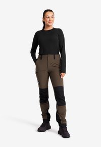 Bruna och svarta utomhusbyxor med slim fit, tillverkade av slitstarkt material. Har flera fickor och förstärkta knäpartier. Svart långärmad tröja.