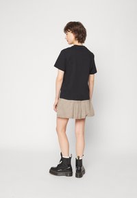 T-shirt noir à manches courtes associé à une jupe plissée beige, mettant en valeur un tissu texturé. Des bottines à lacets noires complètent le look.