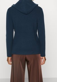 Sweat à capuche bleu marine avec texture côtelée, manches longues et coupe décontractée. Associé à un pantalon large en satin marron.