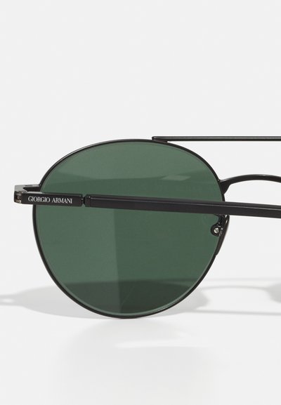 Round sunglasses with dark green lenses, thin black metal frames, and minimalistic design. Features logo on the temple and sophisticated accents.