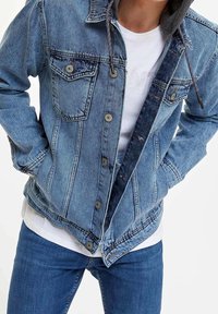 Giacca di jeans con cappuccio grigio scuro, lavaggio azzurro chiaro, chiusura a bottoni, tasche sul petto e una texture leggermente usurata. Indossata sopra una maglietta bianca.