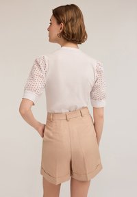 Witte top met mesh-textuur mouwen en beige hoge taille shorts. Beschikt over opgerolde manchetten en een getailleerd ontwerp. Eenvoudige en strakke lijnen.