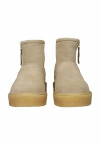 Botas de tobillo de ante beige con puntera redondeada, cremallera en la parte posterior y suela de goma marrón clara. Textura exterior suave y detalles de diseño mínimos.