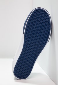 Sneaker bianco con suola in gomma caratterizzata da un motivo di trazione blu e testurizzato. Il materiale superiore appare liscio, accentuato da un design a profilo basso.