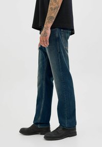 Donkerblauwe, rechte jeans met een vervaagde afwerking, vijf zakken en gestikte details. Gecombineerd met zwarte, platte schoenen.