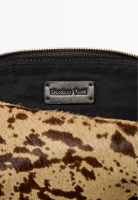 Brązowa tkanina w kropki z czarną podszewką. Posiada skórzaną metkę z wytłoczonym napisem "Massimo Dutti" nad złotym zamkiem błyskawicznym.