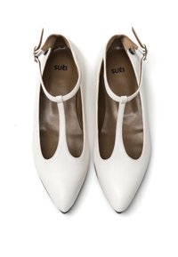 Ballerine bianche a punta con texture a riga, dotate di un design a T e una piccola fibbia sulla caviglia. Rivestimento interno marrone e logo presenti.
