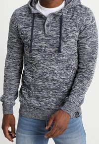 Felpa con cappuccio a maglia marnata nei toni del blu navy e grigio, con stringhe, collo con bottoni e polsini e orlo a costine. Il tessuto appare testurizzato e caldo.