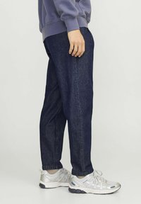 Donkerdenim joggers met een relaxte pasvorm, voorzien van zijzakken en omgeslagen manchetten, gecombineerd met zilverkleurige sportschoenen.