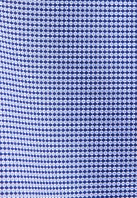 Gros plan sur un tissu avec un motif répétitif de petits carrés bleus et blancs disposés en grille.